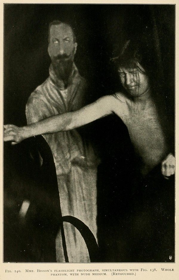 A vintage black and white photograph of a spiritualist séance, featuring a medium and a client in a dimly lit room.