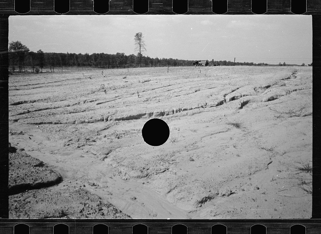 A black and white photograph of a plowed field with a large black hole in the center.