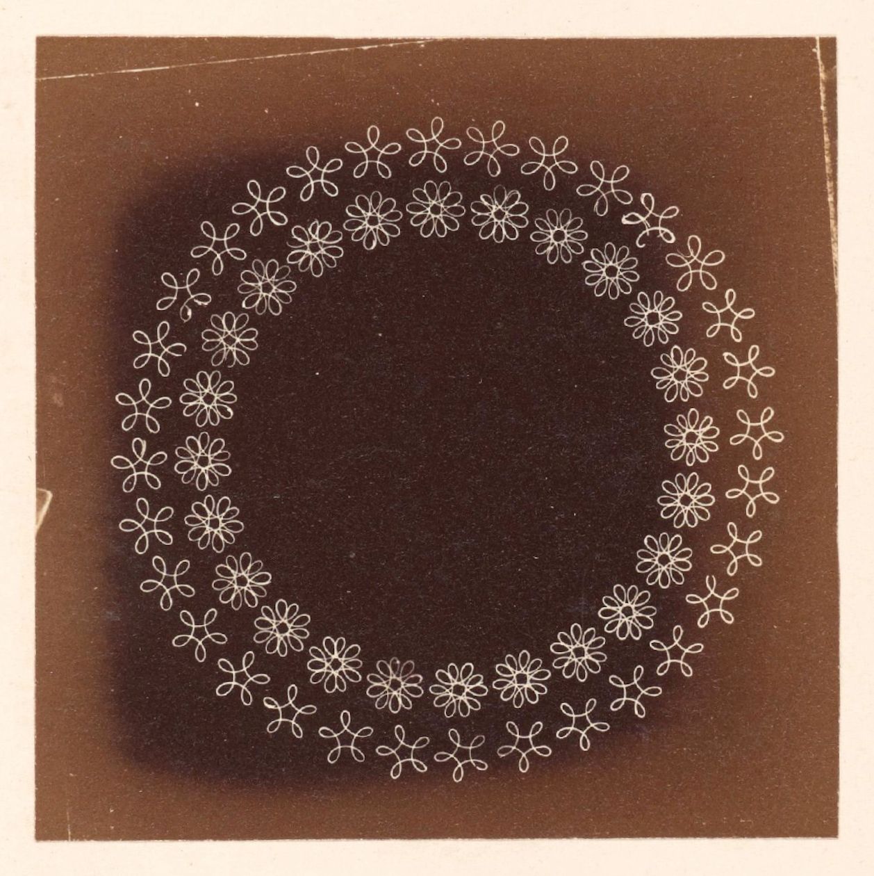 A sepia-toned photograph featuring a circular pattern of delicate floral motifs arranged around a dark center.