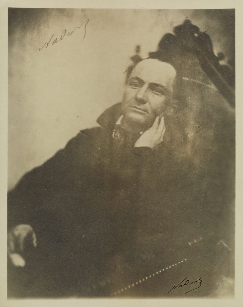 Vintage sepia-toned photograph of a man in a contemplative pose, with signatures in the corners.