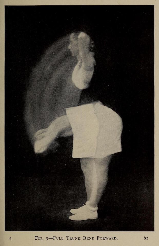 A vintage black and white photograph of a child bending forward, with blurred hair and limbs, against a black background.