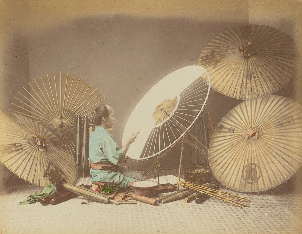A vintage photograph of a Japanese artisan working on paper umbrellas in a traditional workshop setting.