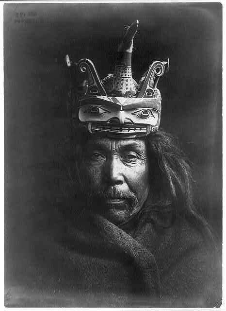 A black and white portrait of an Indigenous man wearing elaborate headgear.