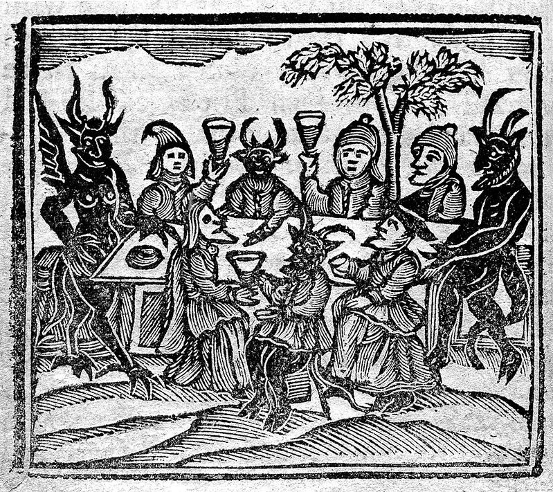 A black and white woodcut illustration depicting a ritualistic scene with humans and demonic figures gathered around a table.