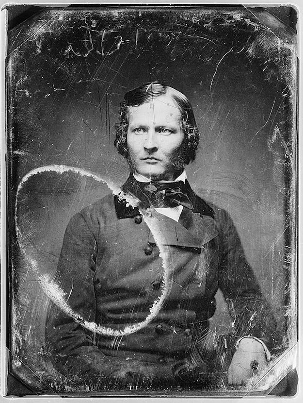 A vintage daguerreotype portrait of a man in a dark coat and bow tie, with a serious expression.
