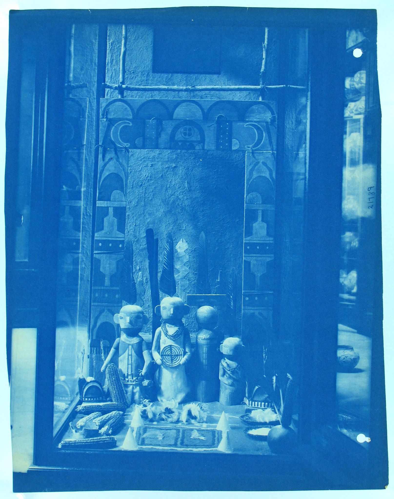 Cyanotype photograph of a display of wooden statues and artifacts within a decorated doorway.