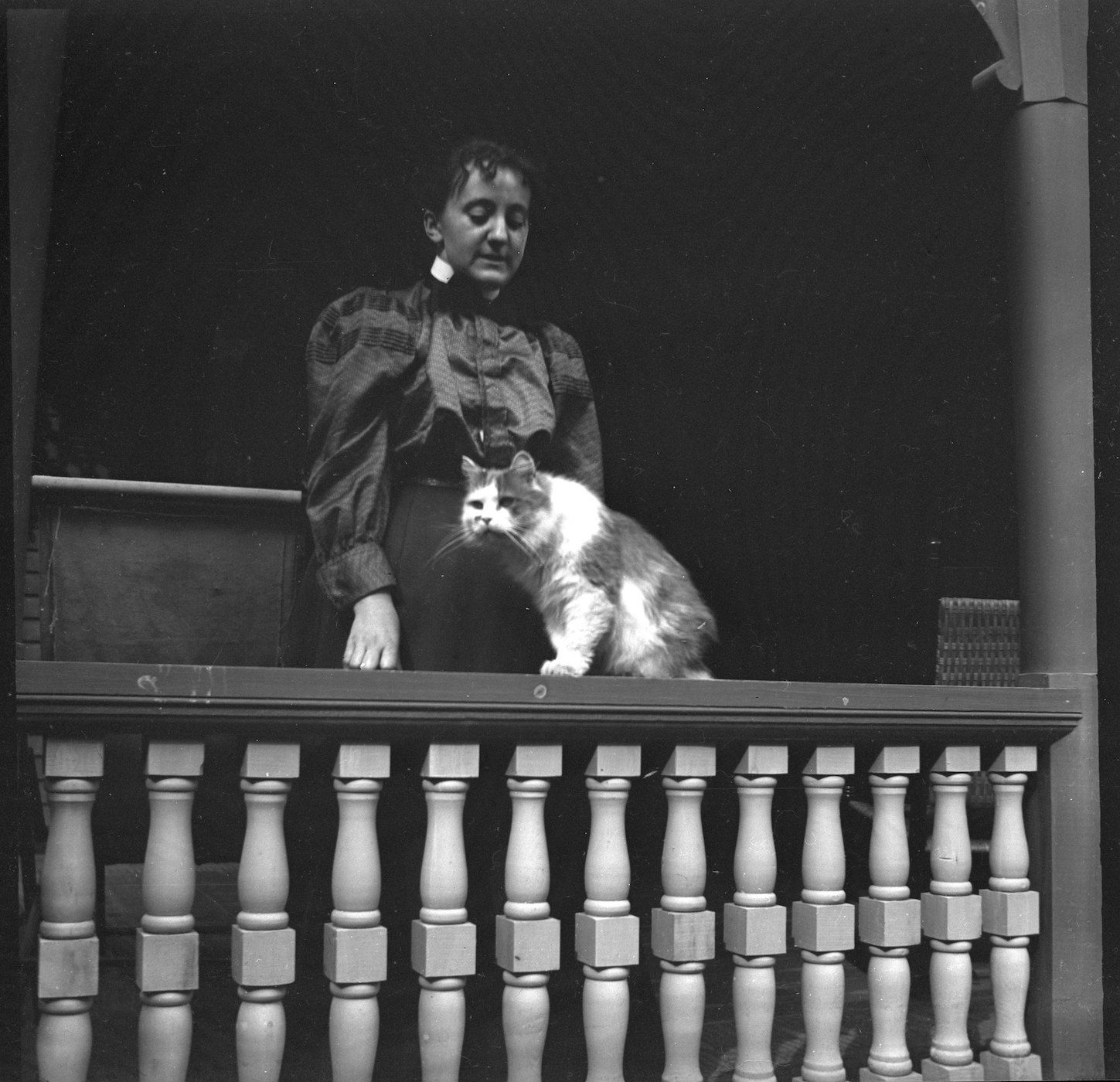 A black and white photograph of a woman and a cat on a balcony.