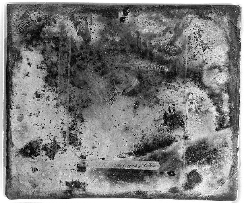 A heavily distressed daguerreotype photograph with a faint cityscape and handwritten text.