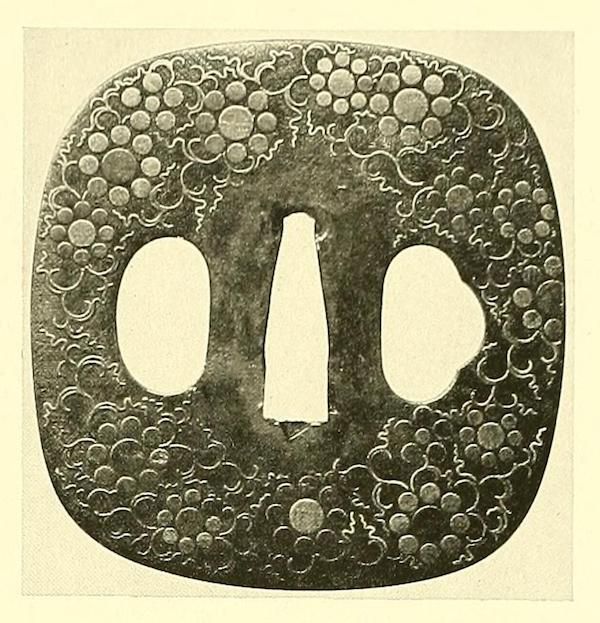 A detailed view of a Japanese tsuba, a sword guard, with a floral pattern and three openings.