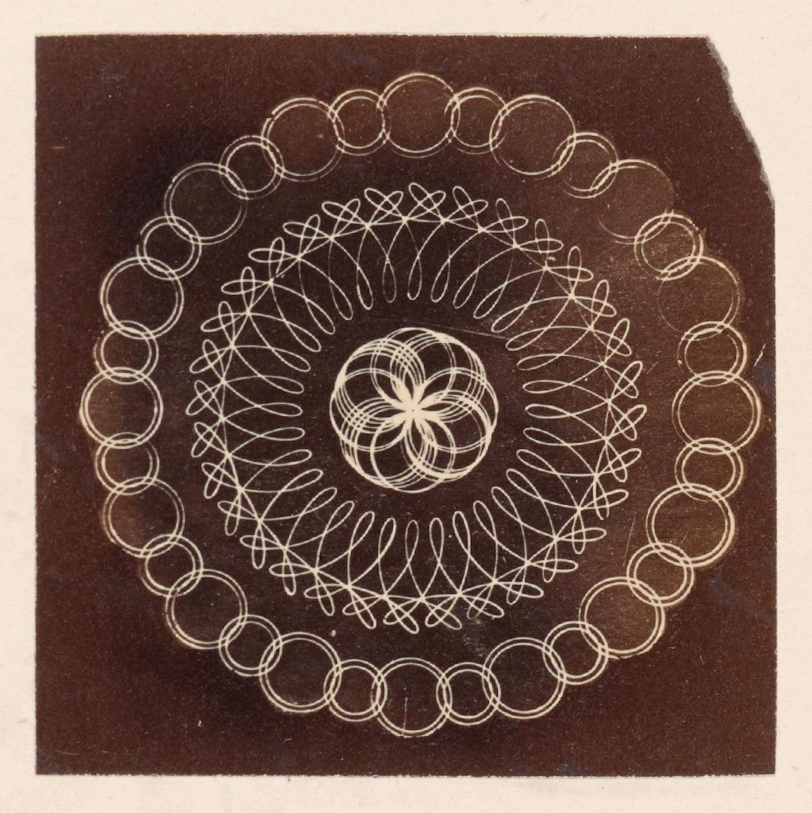 A vintage photogram featuring a complex geometric pattern of looping lines and concentric circles against a dark background.