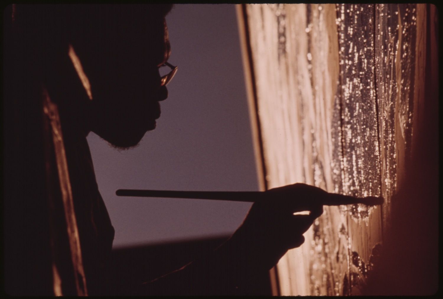 A silhouetted artist painting on a brightly lit canvas.