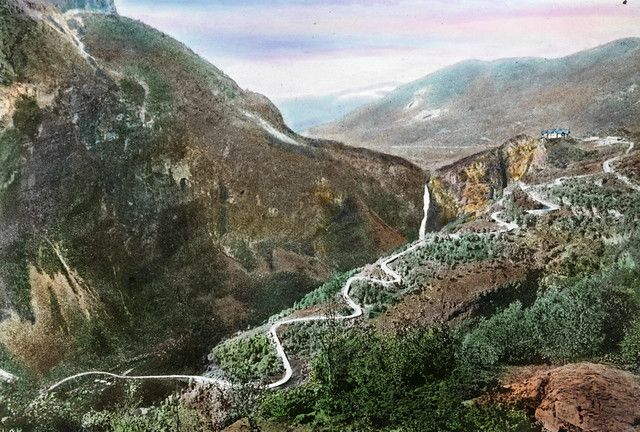 Vintage hand-colored photograph of a winding road through a mountainous landscape.
