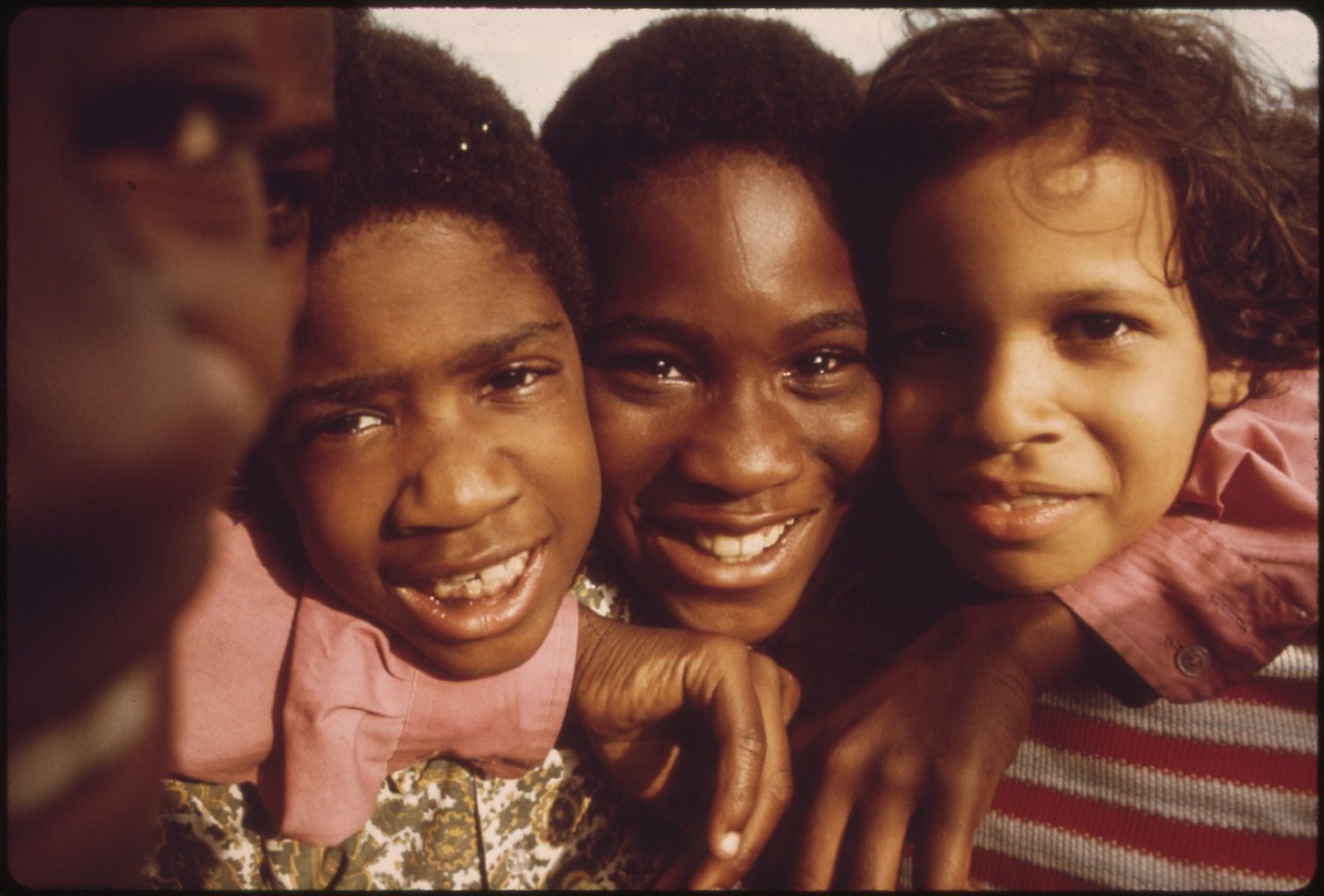 Close-up portrait of three smiling children huddled together.