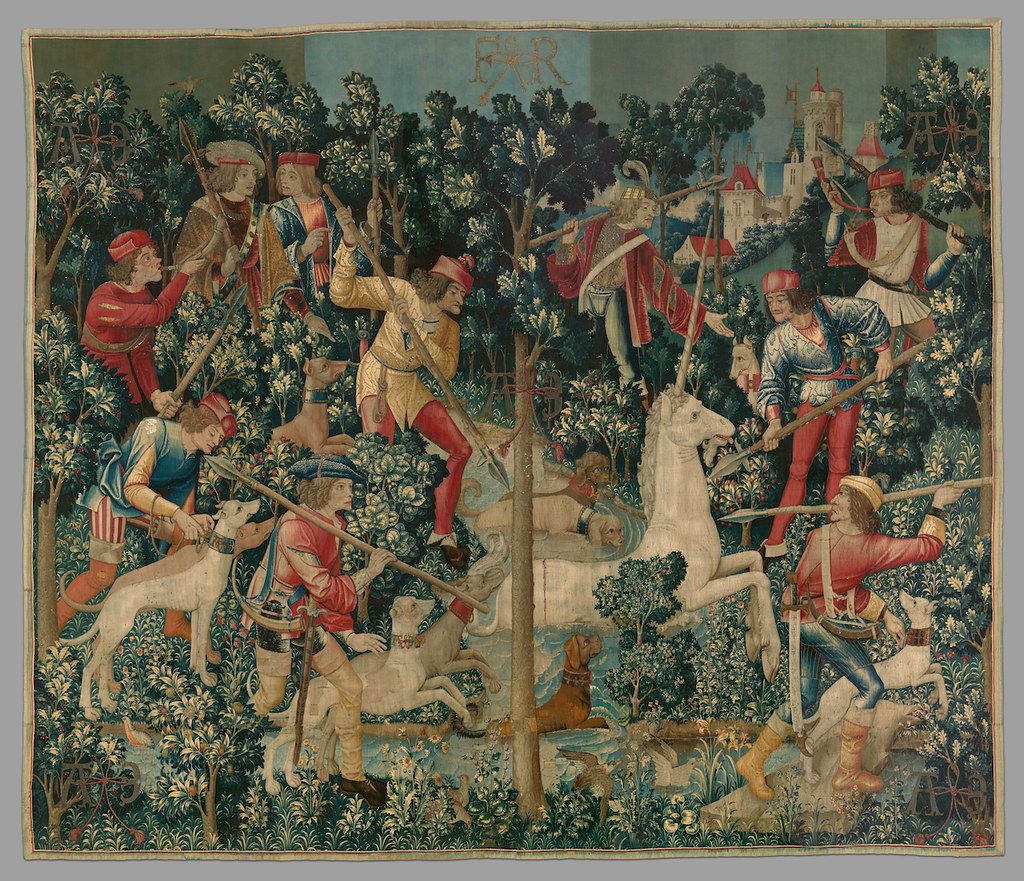 A detailed tapestry depicting a medieval hunting scene with hunters pursuing a white unicorn in a dense forest.