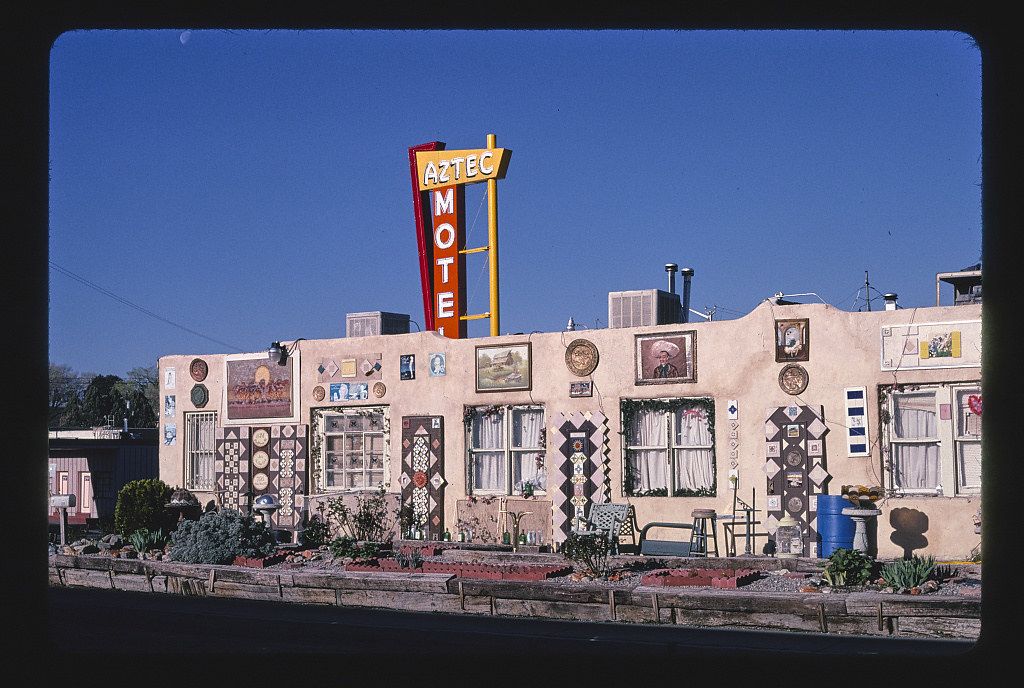 Exterior view of the Aztec Motel, a long, low-rise building covered in artwork, under a clear blue sky.