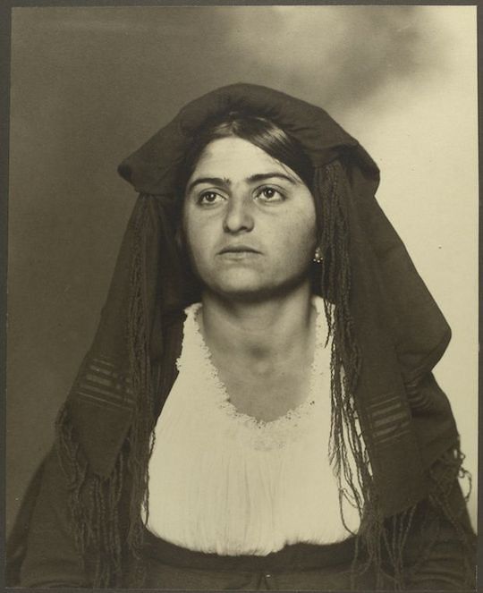 Sepia-toned portrait of a woman wearing a dark head covering with long tassels.
