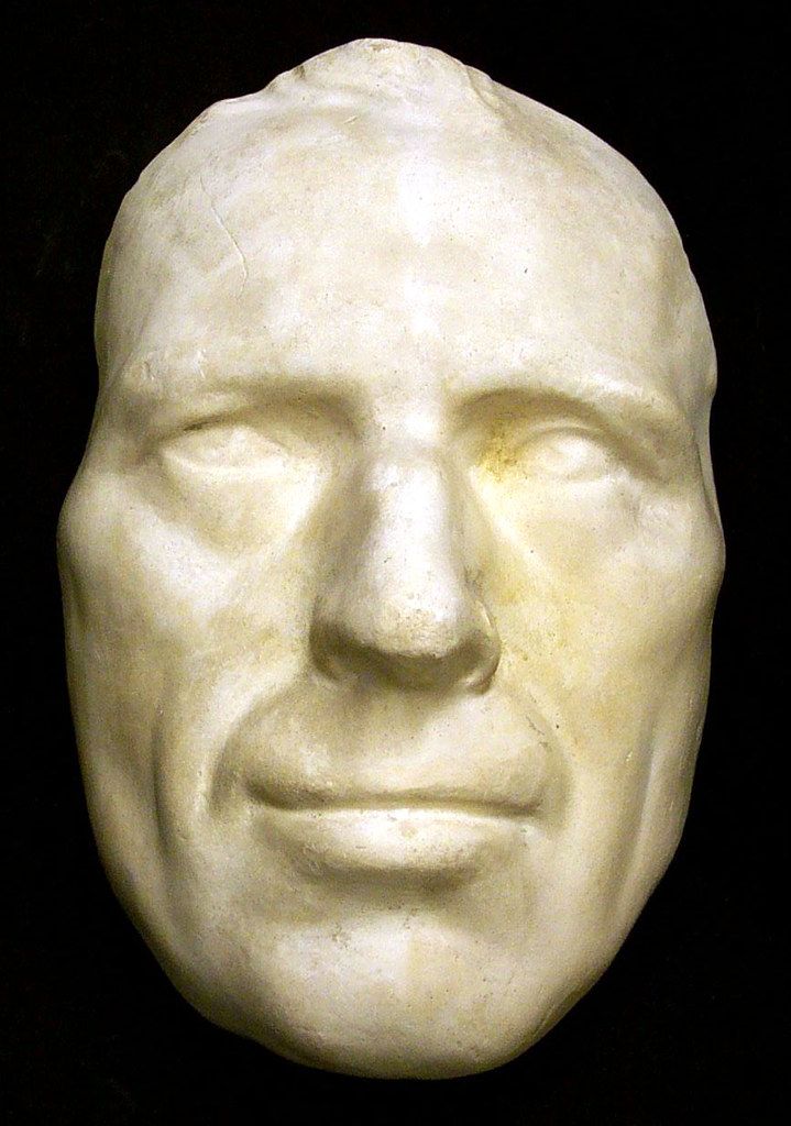 Close-up of a plaster cast of a man's face, showing weathered features and a serene expression.
