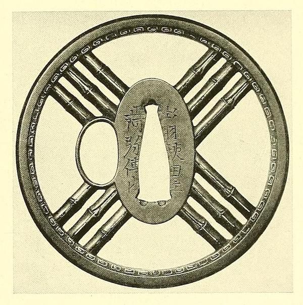 A detailed view of a Japanese tsuba, a sword guard with an intricate openwork design and Japanese characters inscribed in the center.