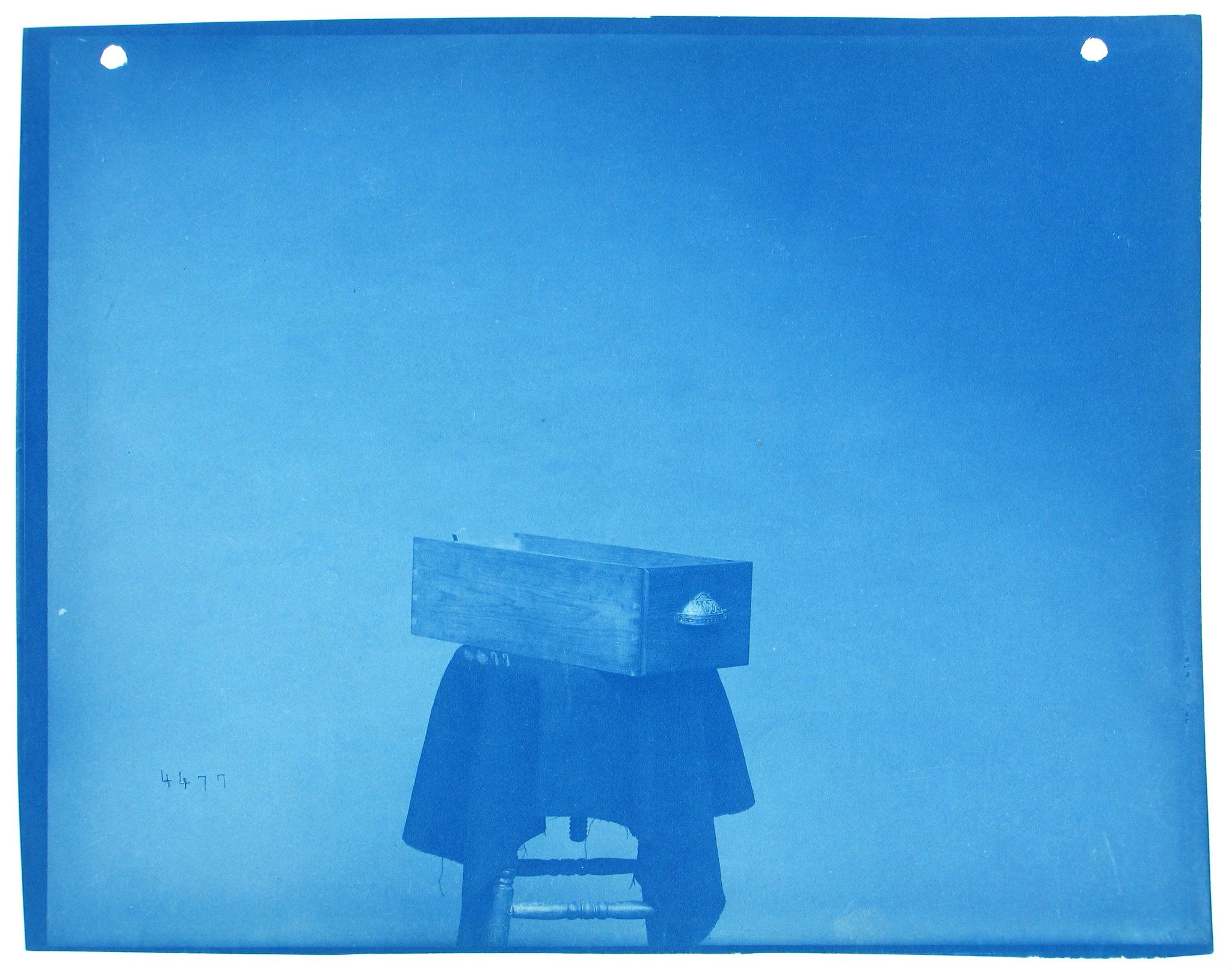 Cyanotype photograph of a person with a box over their head, standing against a blue background.
