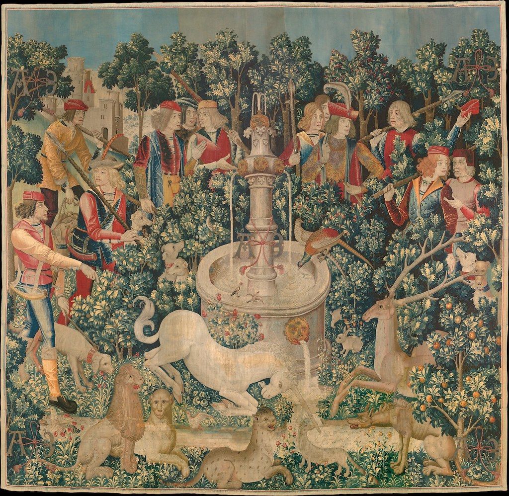 A detailed tapestry depicting a hunting scene with a unicorn, hunters, and dogs in a lush forest setting.
