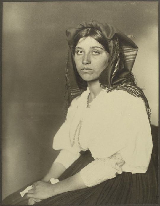 Sepia-toned portrait of a young woman wearing a tall, conical hat and a high-necked blouse.