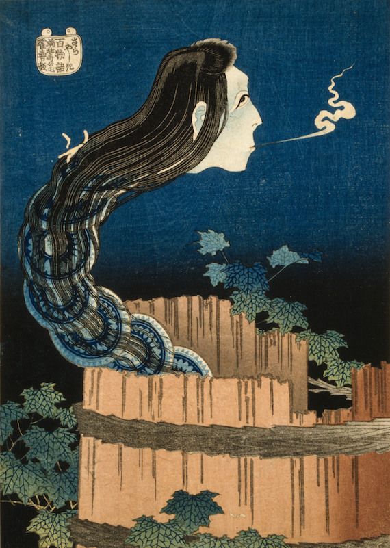 Vintage Japanese woodblock print of a ghostly figure with long hair transforming into a snake, set against a blue background with a stone wall and foliage.