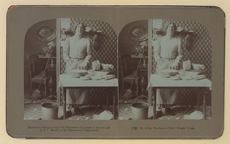 Stereoscopic photograph of a woman in a kitchen, with various kitchen items on a table. The image is sepia-toned and dated 1899.