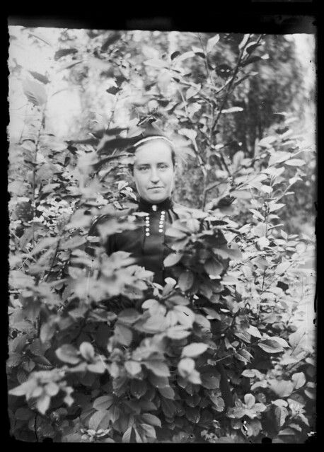 A vintage black and white photograph of a man in uniform standing in a bush.