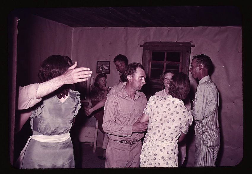 A vintage color photograph of a group of people gathered in a rustic room.