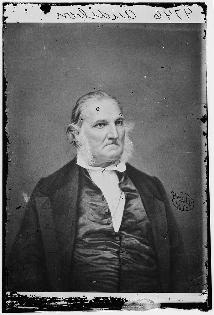 A vintage black and white portrait of a man in a dark jacket and light shirt, taken by photographer Mathew Brady.