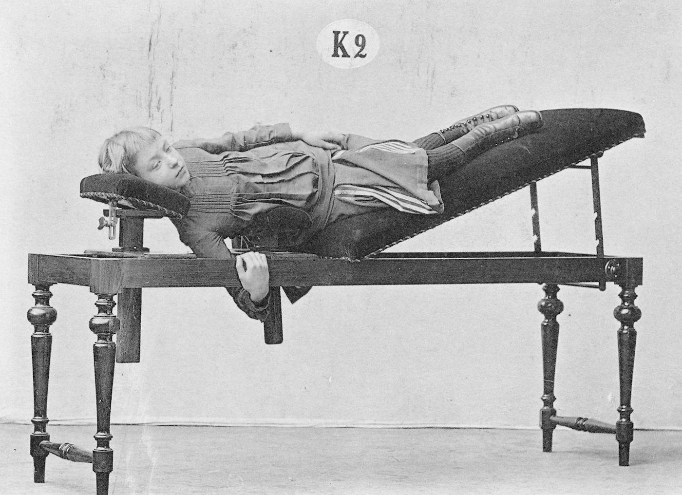 Vintage black and white photograph of a young woman lying on a medical apparatus.