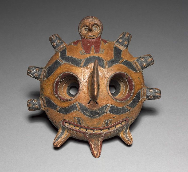 A terracotta mask with a circular shape, featuring stylized facial features and geometric patterns.