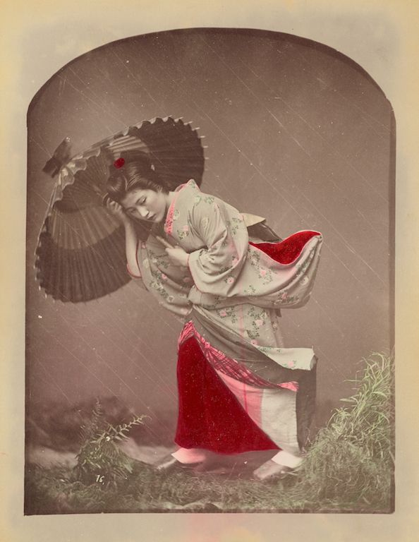 Vintage sepia-toned photograph of a Japanese woman in traditional kimono and holding an umbrella in the rain.