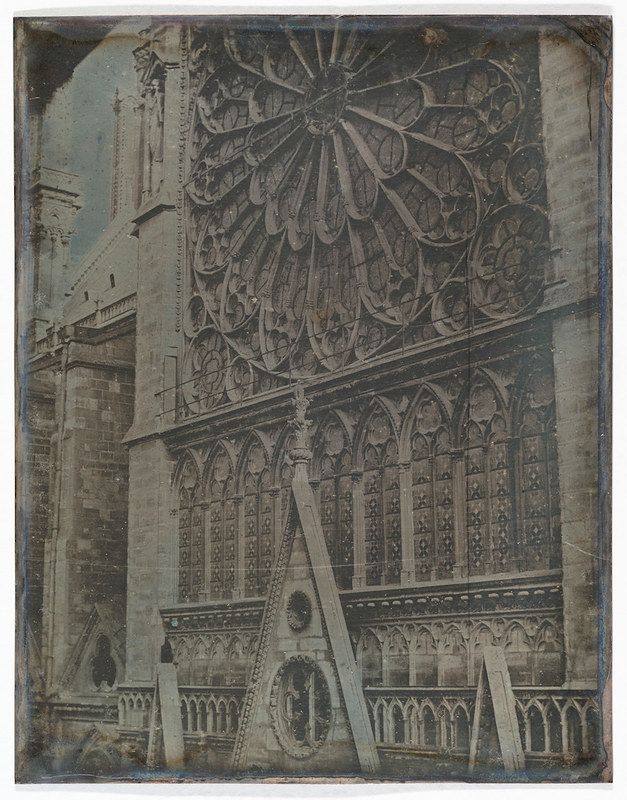 Vintage photograph of a gothic cathedral facade with a rose window and scaffolding.