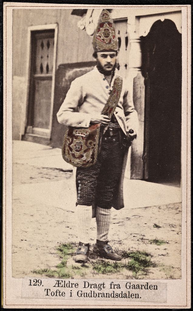 Vintage sepia-toned photograph of a man in traditional Norwegian folk costume standing outdoors.