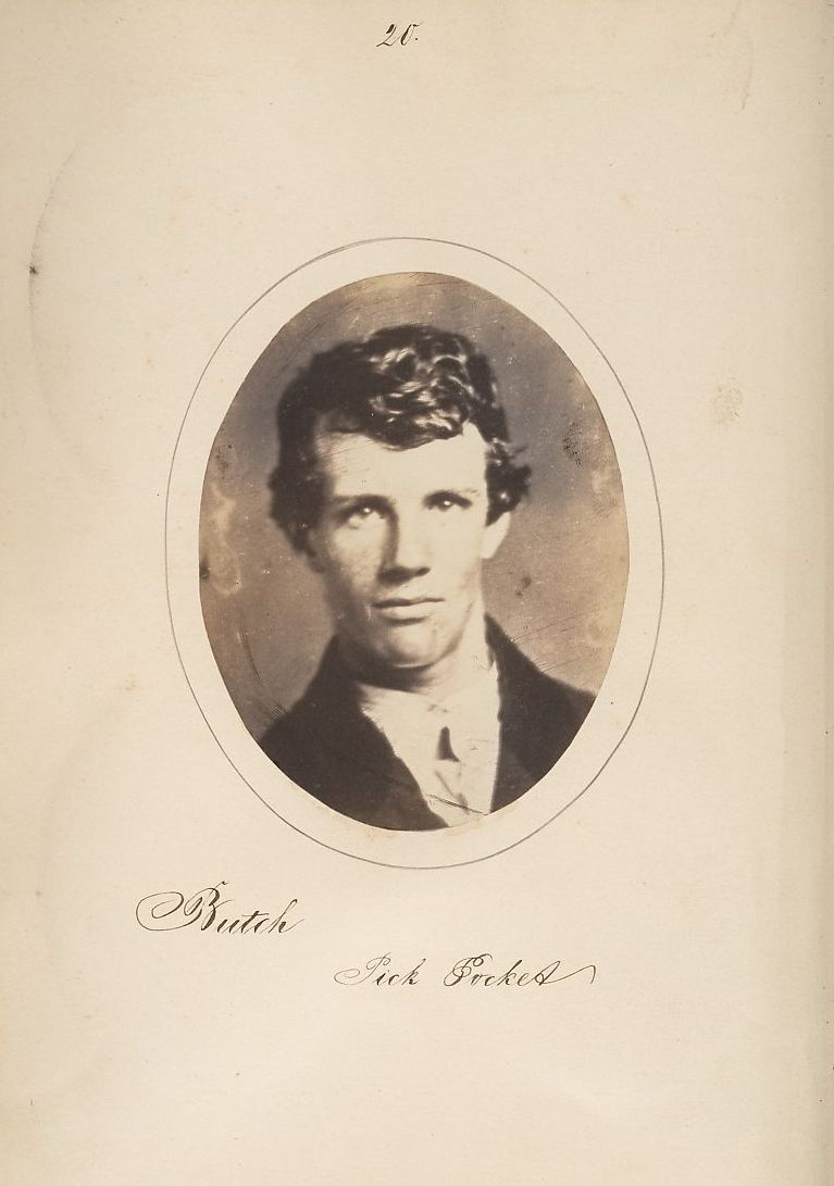 A sepia-toned oval portrait of a man with short wavy hair and a slight smile, wearing a dark coat and light-colored shirt. Below the portrait is handwritten script reading 'Butsche' and 'Sick Erckel'. The number '20' is written in the upper right corner of the page.