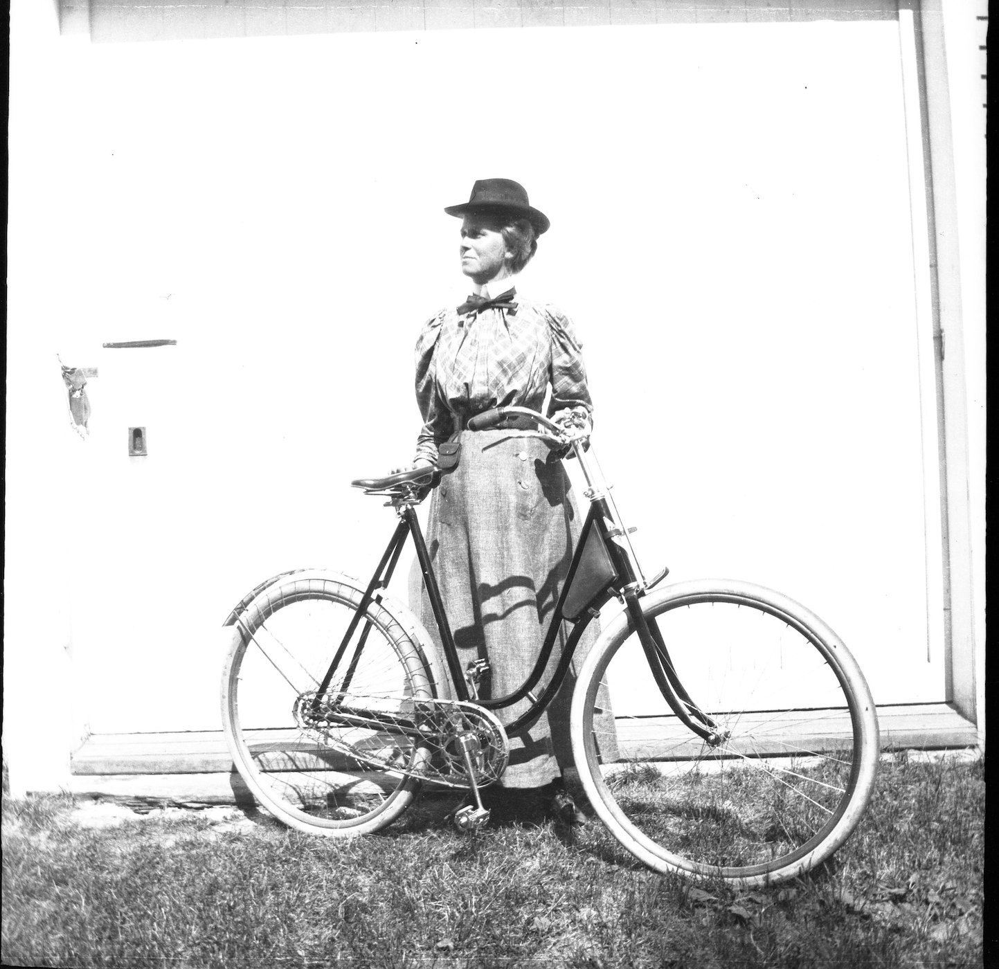 A black and white photograph of a woman standing next to a bicycle.