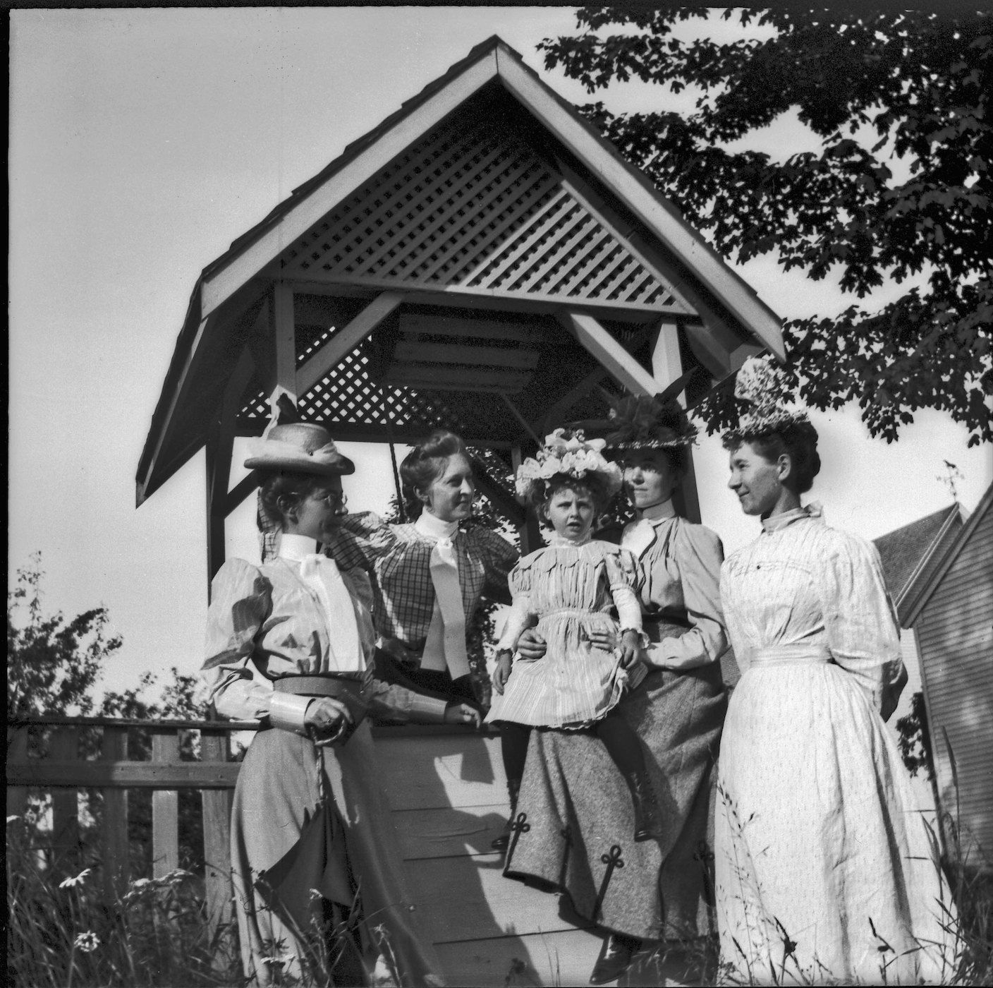 A black and white photograph of six women standing inside a wooden gazebo.