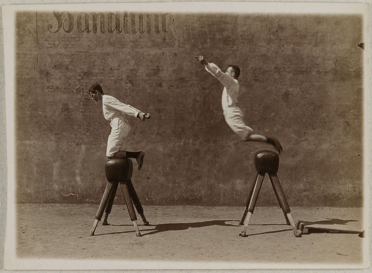 Vintage photograph of two men performing gymnastics on wooden horses.