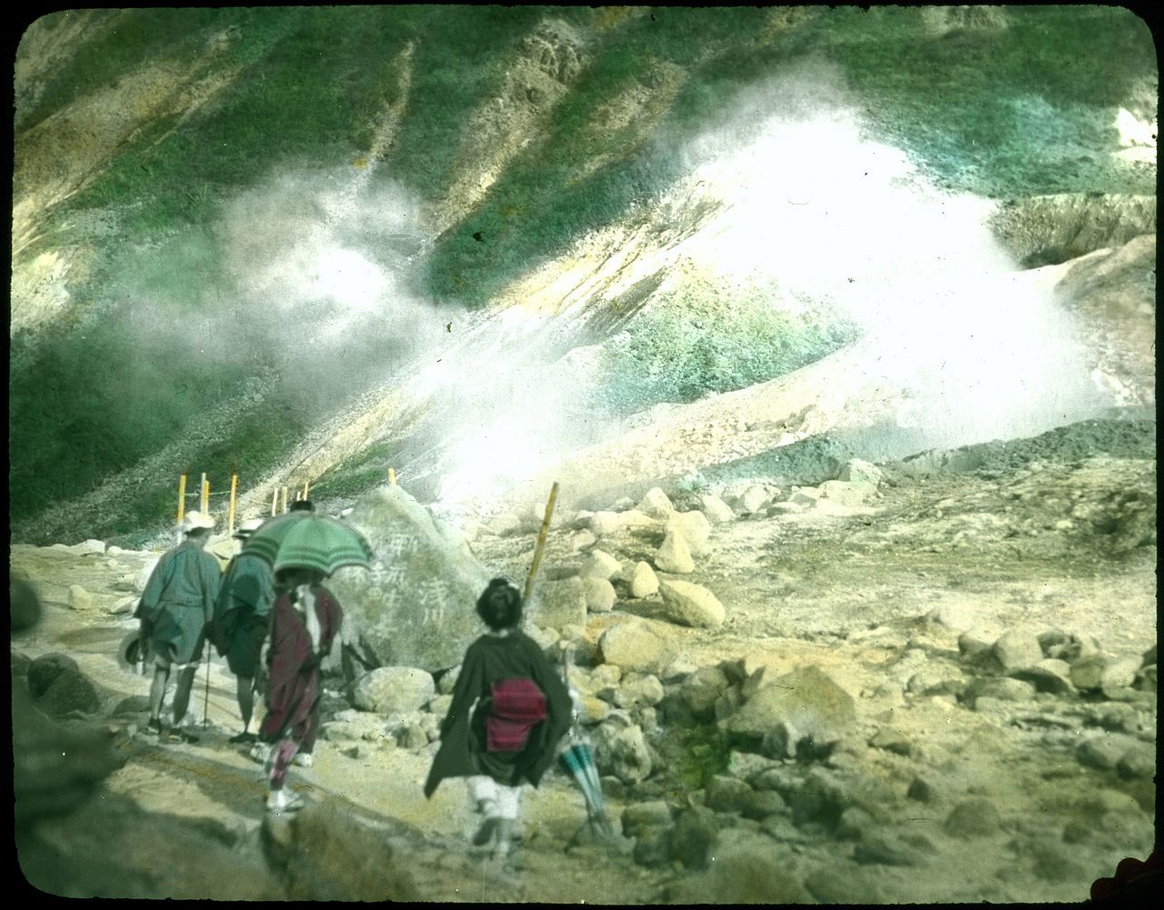 Vintage photograph of a group of people in traditional Japanese clothing traversing a rocky, mountainous landscape.