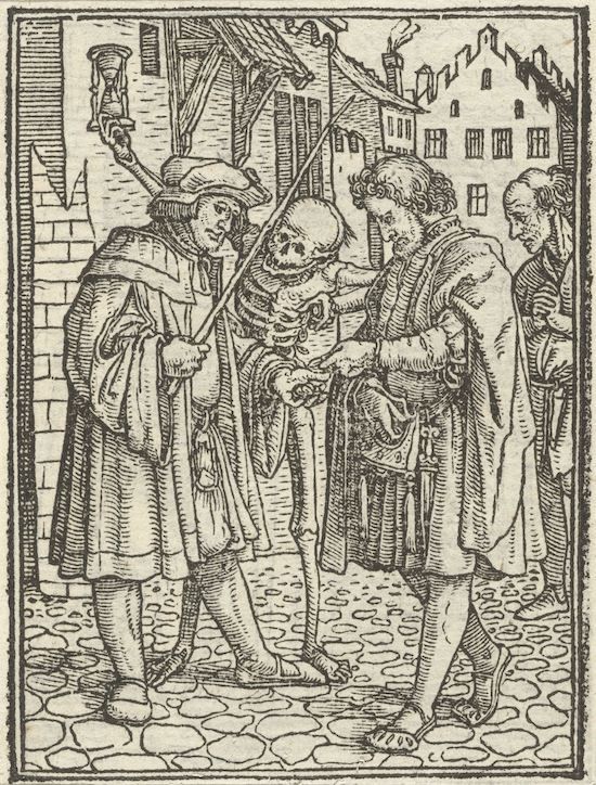 A black and white woodcut illustration depicting a scene with four figures in a town setting. The central figure is a skeleton, dressed in tattered clothing, with a hat on its head. It is being approached by a man holding a torch, who appears to be examining the skeleton. Another man is handing a bag to the skeleton. An older man stands behind them, observing the scene. The background shows a street with buildings, some with windows and chimneys. The street is paved with stones.