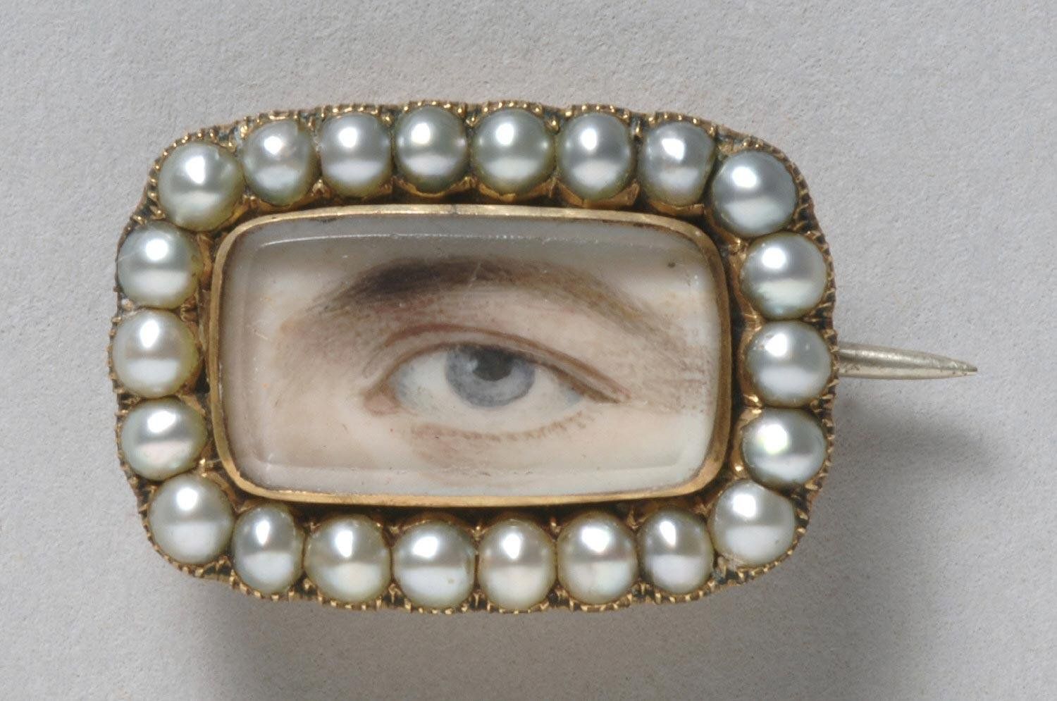 Close-up of a vintage brooch with a painted eye surrounded by pearls.