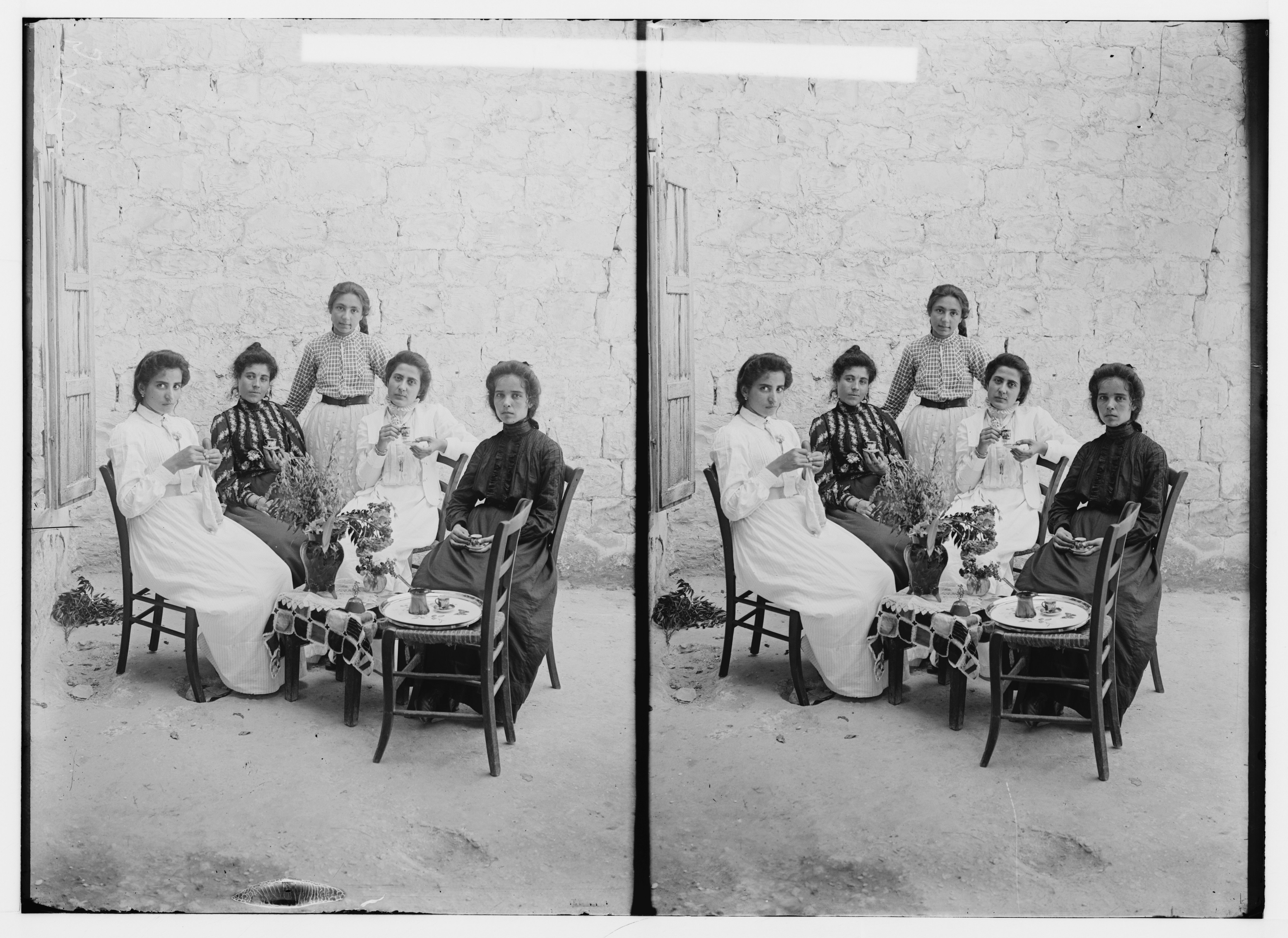 Stereoscopic photograph of five women seated around a table with flowers and food.