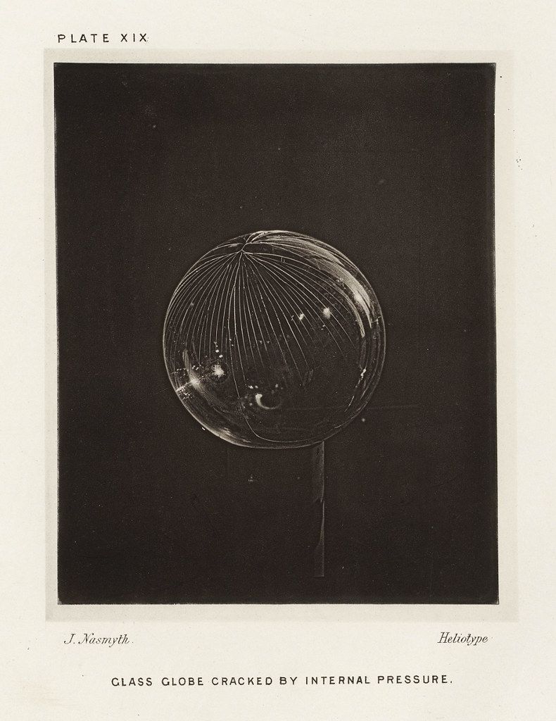 A black and white photograph of a glass globe cracked by internal pressure.