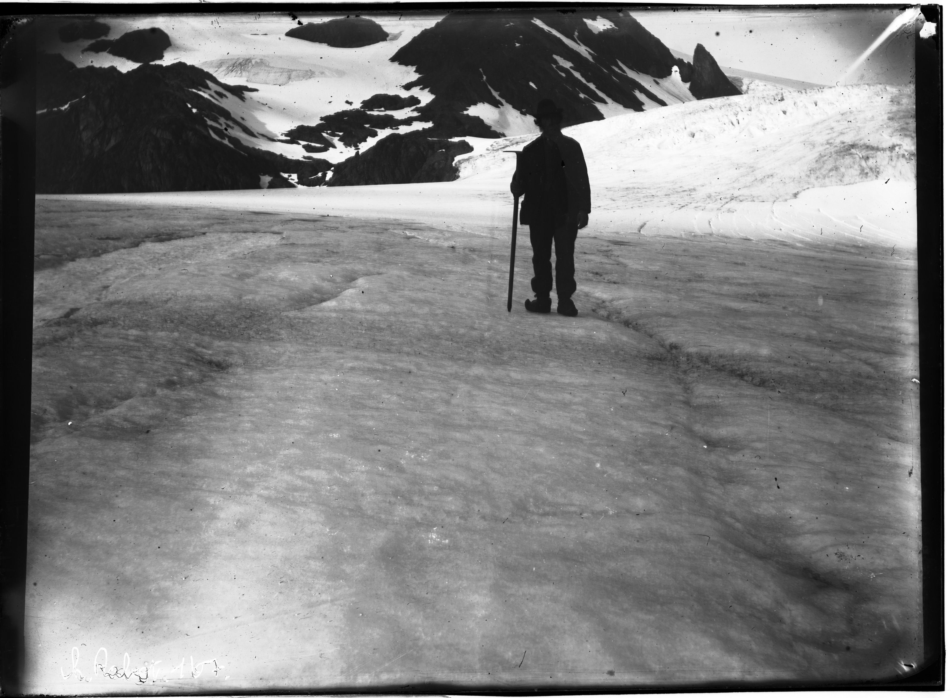 A vintage black and white photograph of a lone figure standing on a vast expanse of snow and ice, with rugged mountains in the background.