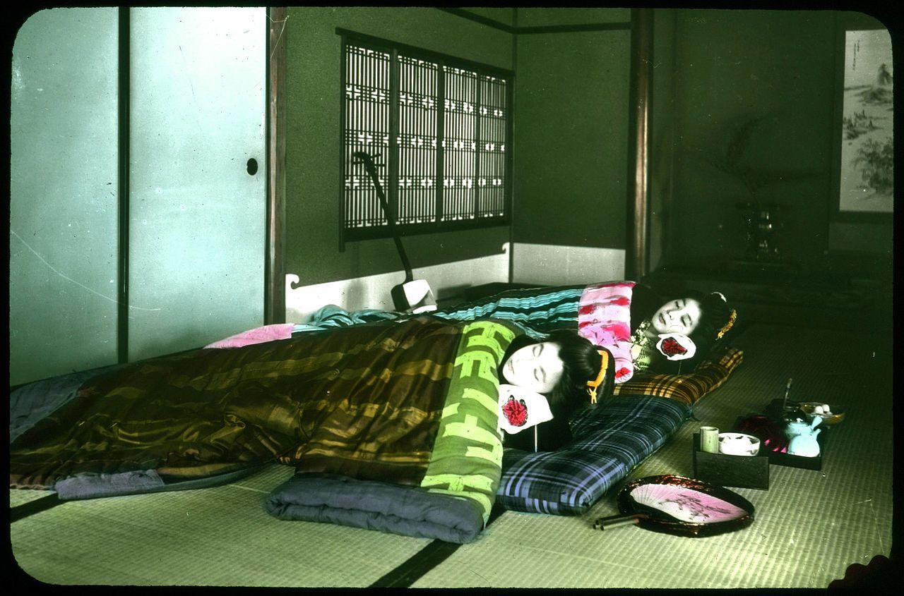 A traditional Japanese room with three people lying on futons, all wearing elaborate white makeup and traditional Japanese clothing.