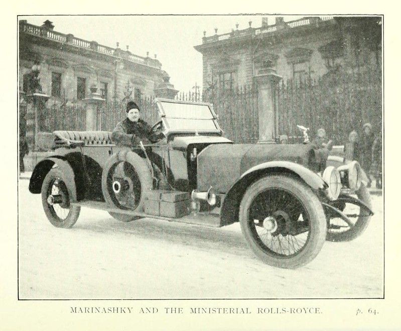Vintage black and white photograph of a Rolls-Royce car with a driver in front of a large building.