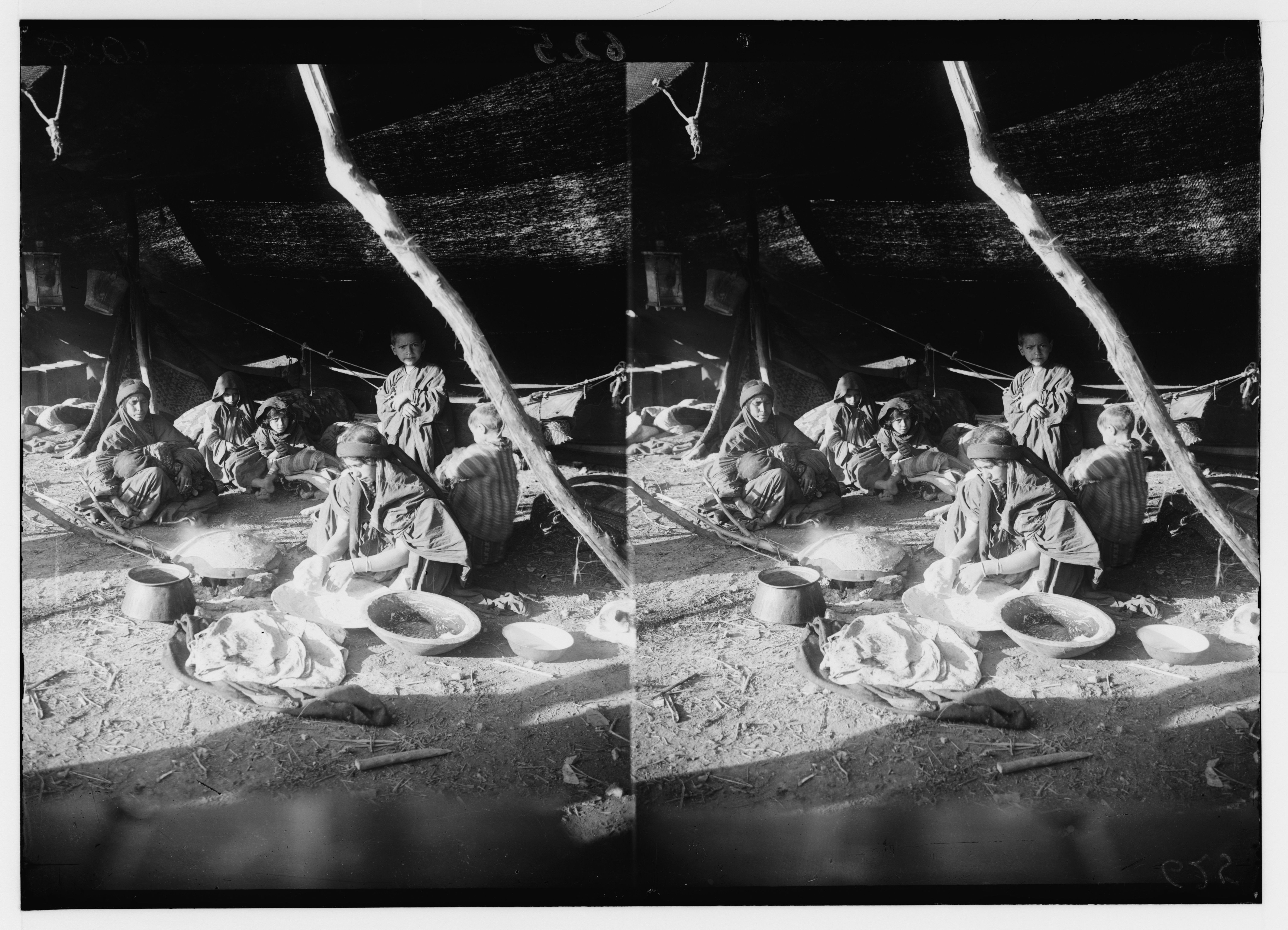 Stereoscopic photograph of a group of people cooking outdoors around a fire, with a makeshift shelter in the background.
