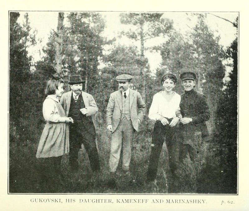 A vintage black and white photograph of five people standing outdoors in a wooded area.