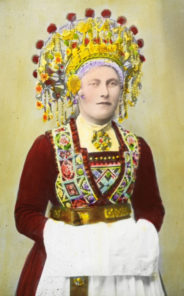 Vintage hand-colored portrait of a woman in traditional folk attire with elaborate headwear and embroidered dress.